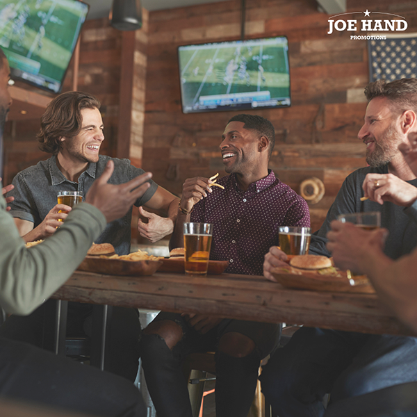 Friends share food and beers while a football game plays on the TVs overhead in a busy sports bar.